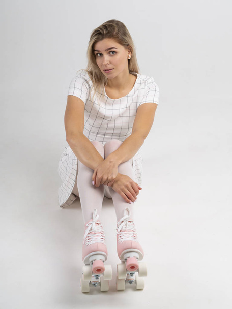 Atrakcyjna dziewczyna w rocznika quad rolki siedzi na podłodze patrząc w kamerę i flirtuje na białym tle - Zdjęcie, obraz