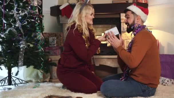 Side view of smiling Caucasian blond woman giving Christmas present to her adorable husband or boyfriend. Surprised man hugging his soulmate. New Years eve, celebration, holidays season. - Materiaali, video