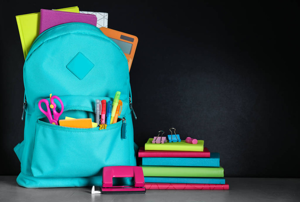 Bright backpack with school stationery on grey stone table against black background - Foto, imagen