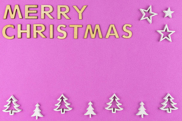 L'inscription Joyeux Noël fait de lettres en bois, couché à plat d'en haut, isolé sur un fond rose, rugueux. Arbres de Noël en bois blanc disposés en rangée au bas
. - Photo, image