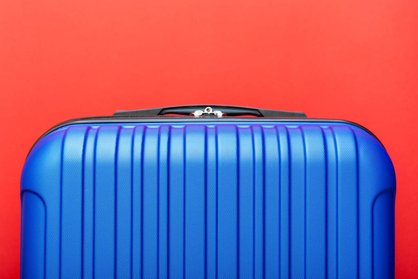 Modern blue suitcase on red background close up with copy space for text. Minimal style travel concept. Vacation trip. Summer holiday stock photo. Trendy color 2020 classic blue - Zdjęcie, obraz