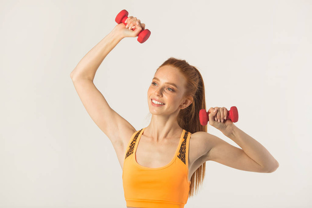 beautiful young woman with red hair with dumbbells in hands on a white background - Фото, зображення