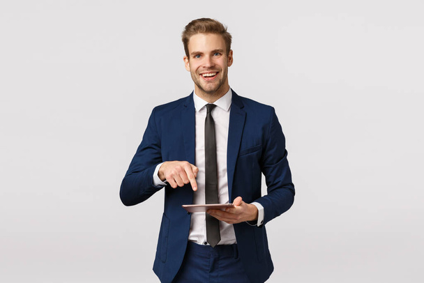 Dit moet je zien. Vrolijke elegante mannelijke ondernemer in klassiek pak, stropdas, met digitale tablet en wijzend gadget scherm om zakenpartner fantastisch nieuws geschreven online magazine te tonen - Foto, afbeelding
