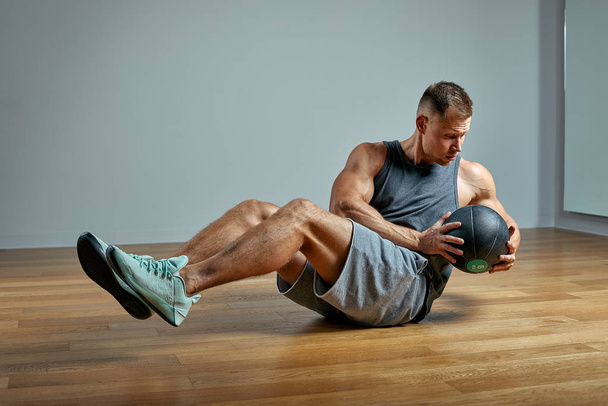 Vahva mies treenaa lääkintäpallon kanssa. Kuva ihmisen täydellinen ruumiinrakenne harmaalla pohjalla. Vahvuus ja motivaatio
. - Valokuva, kuva