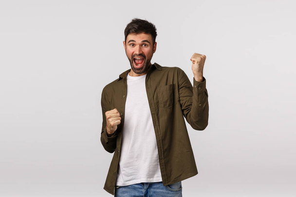 Relish, celebration and victory concept. Cheerful triumphing lucky businessman, guy winning, achieve prize or goal, have great news, fist pump and smiling, become champion, white background - Photo, Image