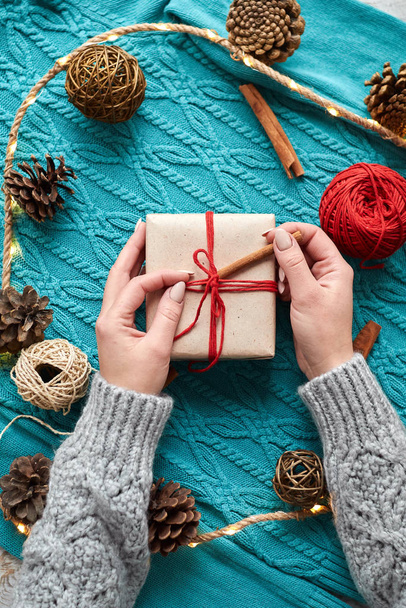 Female's hands in pullover holding Christmas gift box decorated with evergreen branch. Preparion for december holidays - Foto, Imagem