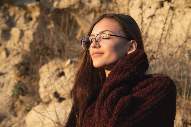 Közelkép portré az érzéki barna lány szemüvegben áll a napon csukott szemmel - Fotó, kép