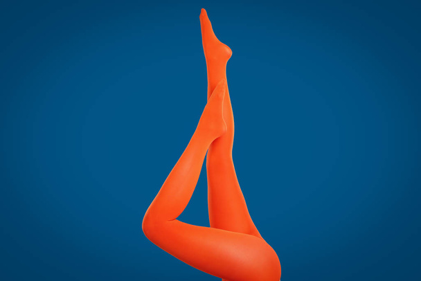 Woman wearing orange tights on blue background, closeup of legs - Valokuva, kuva