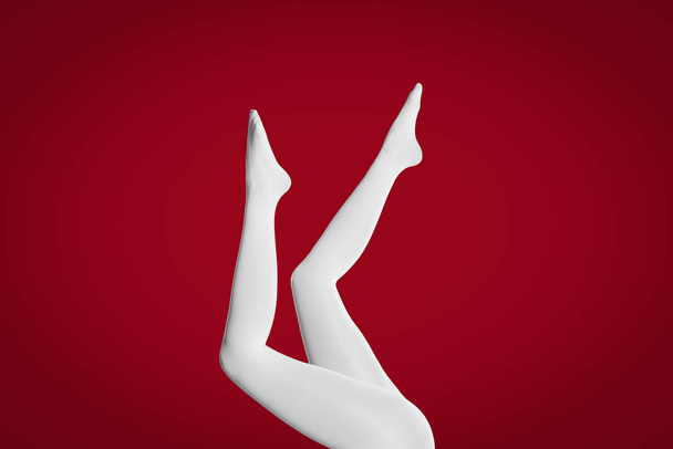 Woman wearing white tights on red background, closeup of legs - 写真・画像