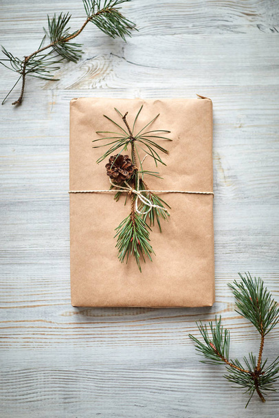 cadeauverpakking voor een boek of laptop in ambachtelijk papier gebonden met touw en versierd met een dennenboom met een kegel  - Foto, afbeelding