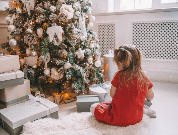pretty little girl near the new year tree. beautiful girl in dress near Christmas tree waiting for holiday. little Princess - Zdjęcie, obraz