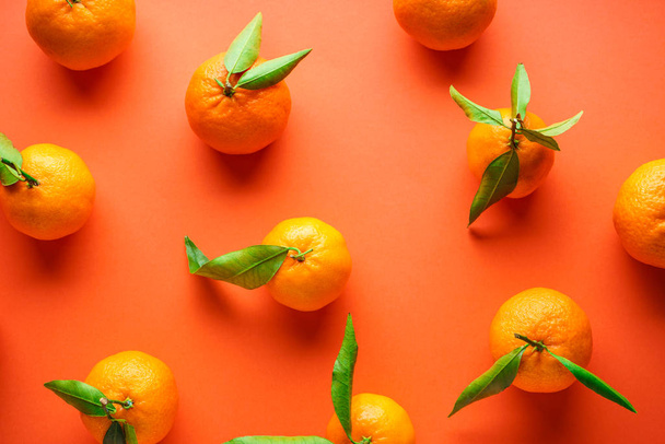 Verse sinaasappelmandarijnen met bladeren, op een oranje achtergrond, plat gelegd. - Foto, afbeelding
