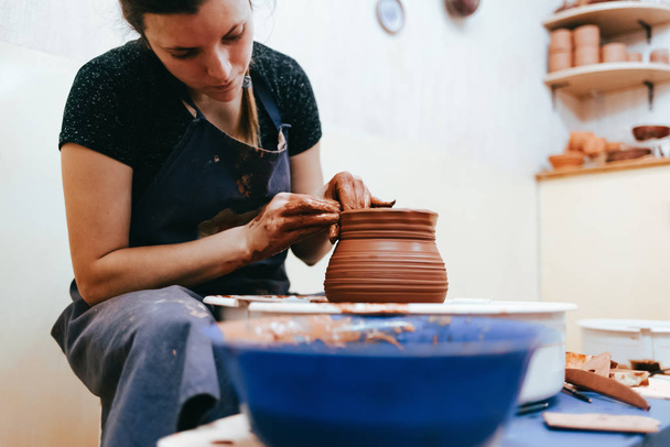 Woman is engaged of pottery. Potter behind the potter's wheel forms clay to create ceramic dishes - Photo, Image