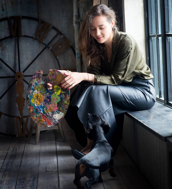 Taiteilija nainen istuu lähellä ikkunaa mäyräkoira
 - Valokuva, kuva