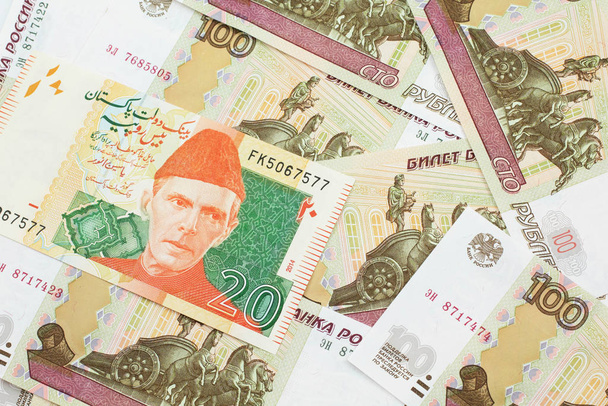 Una imagen de cerca de un billete de banco de 20 rupias pakistaníes naranja y verde con billetes rusos de cien rublos en macro
 - Foto, Imagen