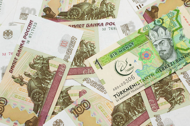 Ένα τραπεζογραμμάτιο ενός μανάτ από το Τουρκμενιστάν κλείνει σε μακροοικονομική βάση με μια συλλογή ρωσικών εκατοντάδων ρουβλίων τραπεζογραμματίων.. - Φωτογραφία, εικόνα