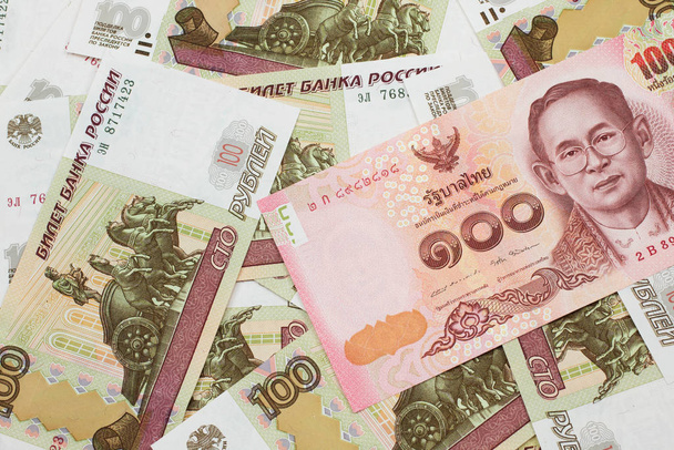 Una imagen de cerca de un billete rojo de cien baht de Tailandia con billetes rusos de cien rublos en macro
 - Foto, Imagen