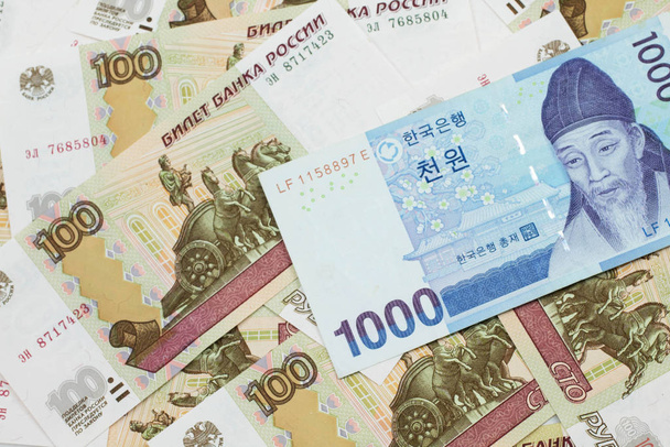 Un bleu sud-coréen mille billets de banque gagné fermer en macro sur un fond de billets de banque russes cent roubles
 - Photo, image