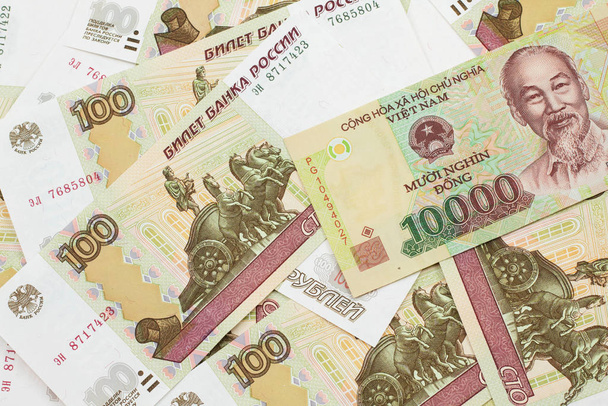A close up image of a Vietnamese ten thousand dong bank note on a background of Russian one hundred ruble bills in macro - Photo, Image