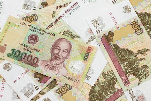 ein Nahaufnahme-Bild einer vietnamesischen Zehntausend-Dong-Banknote auf einem Hintergrund russischer Hundert-Rubel-Scheine in Makro - Foto, Bild