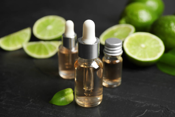Lime essential oil and cut citrus fruits on black table - Foto, imagen