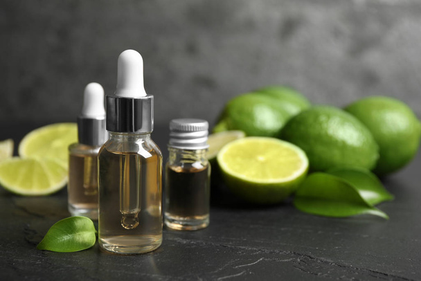 Lime essential oil and cut citrus fruits on black table - Fotoğraf, Görsel