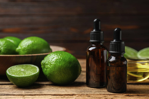 Lime essential oil and cut citrus fruits on wooden table - Fotó, kép