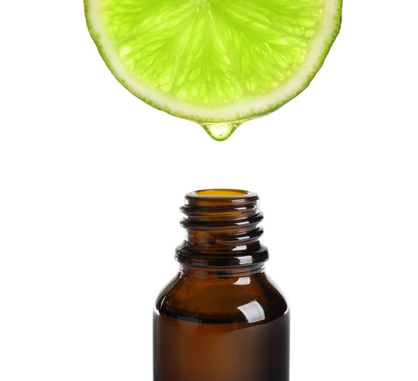 Essential oil dripping from lime slice into bottle isolated on white - Photo, Image