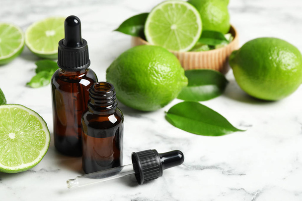 Lime essential oil and citrus fruits on marble table - Zdjęcie, obraz