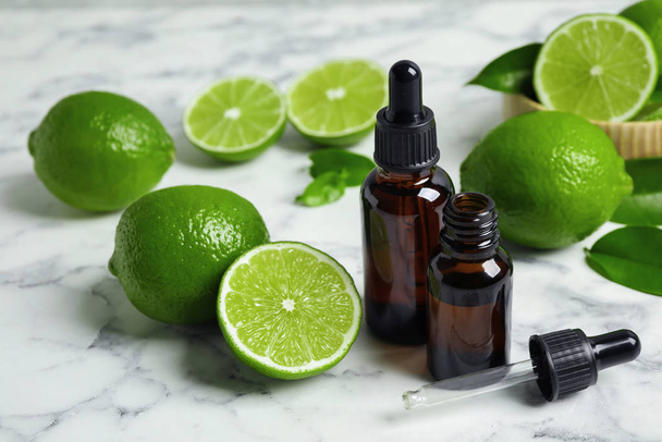 Lime essential oil and citrus fruits on marble table - Zdjęcie, obraz