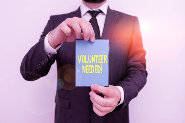 Word writing text Volunteer Needed. Business concept for asking demonstrating to work for organization without being paid Male human wear formal work suit office look hold notepaper sheet use hand. - Photo, Image