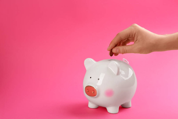 Woman putting coin into piggy bank on pink background, closeup. Space for text - Фото, зображення