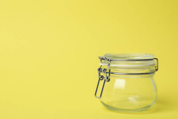 Closed empty glass jar on light yellow background, space for tex - Фото, зображення