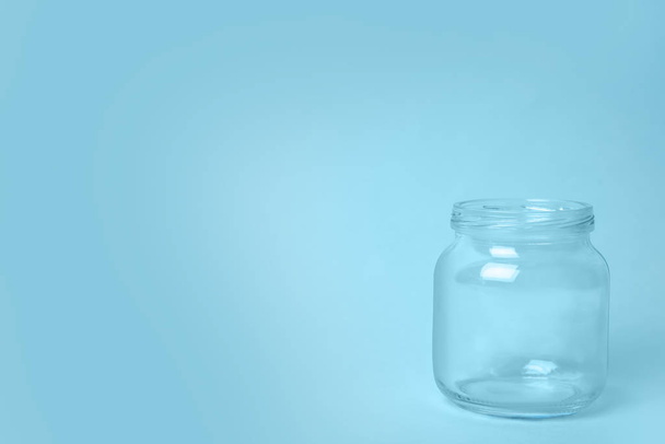Open empty glass jar on light blue background, space for text - Foto, Bild