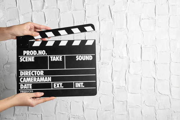 Woman holding clapperboard against white textured wall, closeup with space for text. Cinema production - Foto, imagen