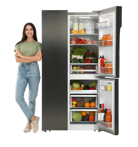 Nuori nainen lähellä avointa jääkaappia valkoisella taustalla
 - Valokuva, kuva