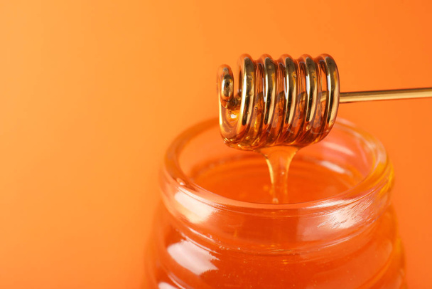 Jar of organic honey and dipper on orange background, closeup. S - Zdjęcie, obraz