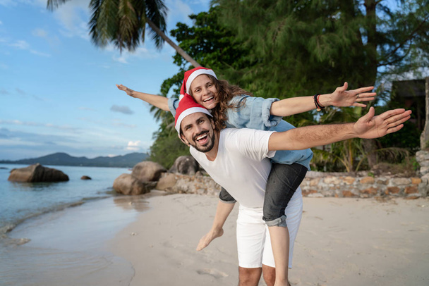 Young beautiful couple in Santa Claus hats walks along the shore - Foto, Imagen