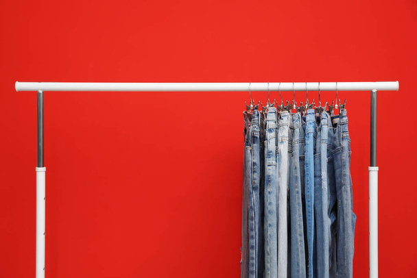 Rack with stylish jeans on red background - Фото, зображення