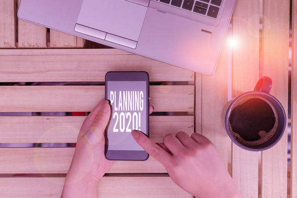 Текстовый знак "Планирование 2020". Концептуальный фотопроцесс создания планов на следующий год женщина компьютер смартфон напиток кружка офис поставляет технологические устройства
. - Фото, изображение