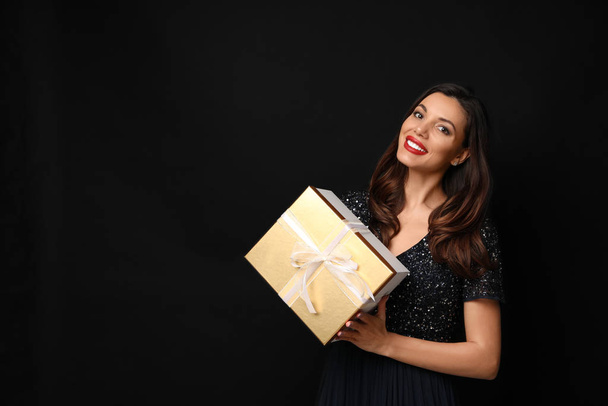 Beautiful woman with Christmas gift on black background - Photo, image