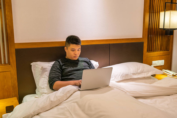 Asian man using laptop on the bed at night - Fotó, kép