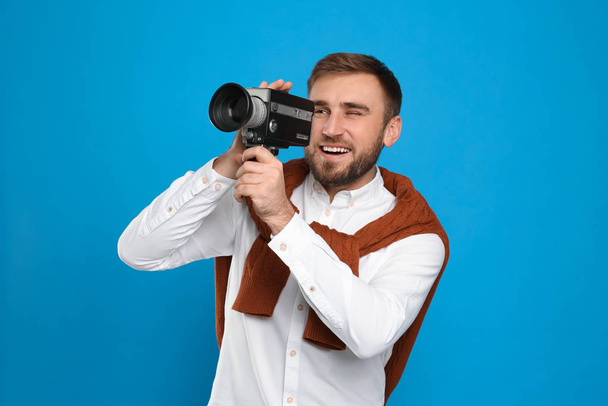 Young man with vintage video camera on light blue background - Fotoğraf, Görsel