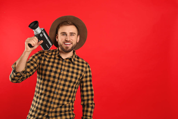 Young man with vintage video camera on red background. Space for text - Foto, imagen
