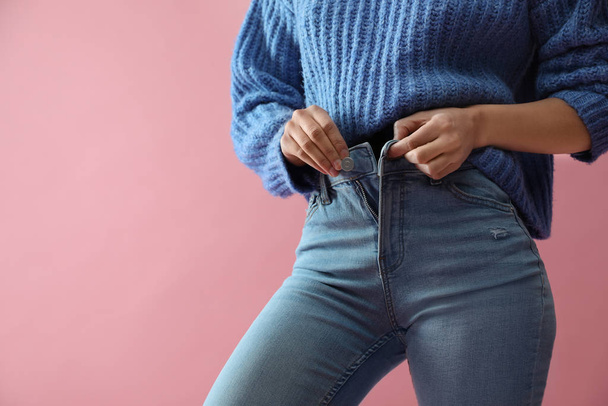 Woman unbuttoning jeans on pink background, closeup - 写真・画像
