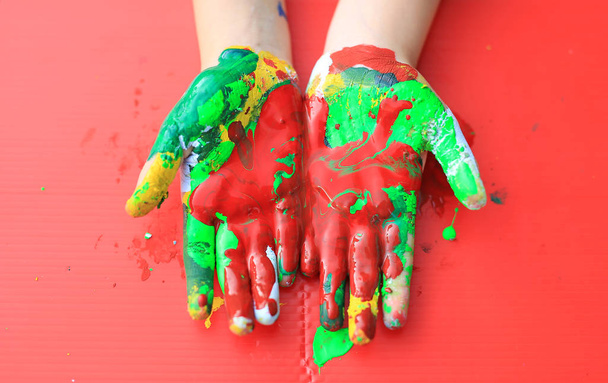 Close-up baby hands with colorful fingers painted over red background. - Zdjęcie, obraz