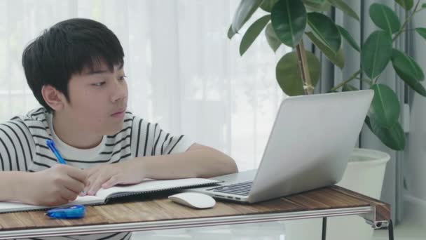 Asian teen boy doing your homework with laptop computer at home. - Кадри, відео