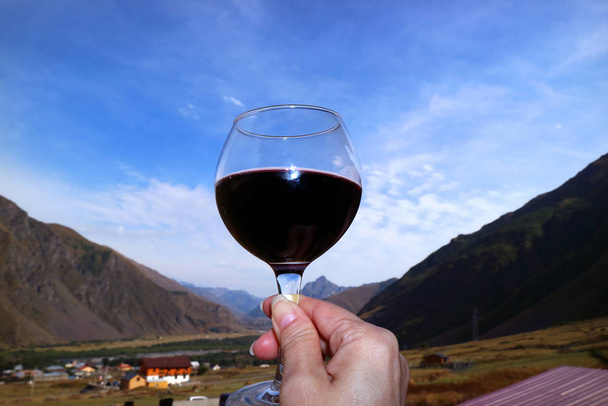 Κοντινό χέρι γυναίκας κρατώντας ένα ποτήρι κόκκινο κρασί κατά Blue Sky - Φωτογραφία, εικόνα