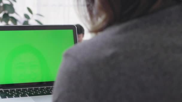 Over the shoulder shot of Asian woman looking at green screen. Office person using laptop computer with laptop green screen, 4K dolly shot - Materiał filmowy, wideo