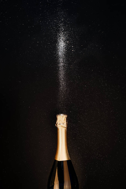 Пляшка шампанського з золотими бризками, блищить на ігристий чорний фон. Пласка лежала. Концепція мінімальної різдвяної зимової вечірки
 - Фото, зображення